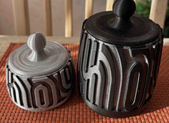 zwei Dosen mit Deckel, eine kleine silberne Dose mit schwarzem Muster und eine große schwarze Dose mit silbernem Muster